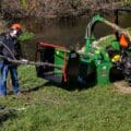 Wallenstein PTO wood chipper green color with man inserting branches into chipper